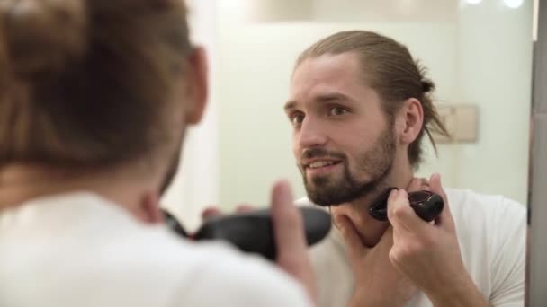 Hombre afeitarse la cara con trimmer mirando en espejo — Vídeos de Stock