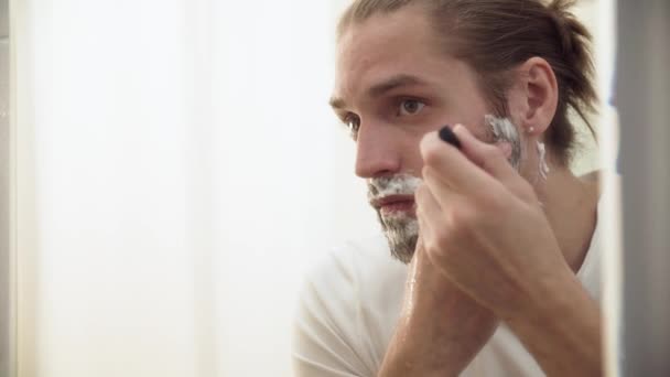 Мужчина бреет бороду с бритвой в ванной комнате — стоковое видео
