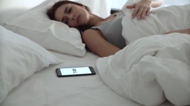 Telefon çalar saat. Yorgun kadın up yatak odası, yatakta uyanma