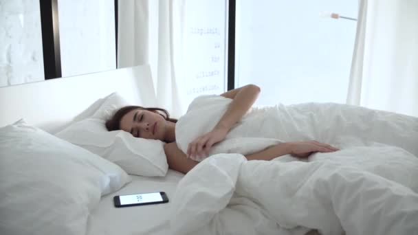 Будильник на телефоне. Женщина спит в постели с белым бельем — стоковое видео