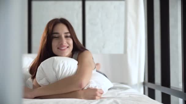 Hermosa mujer acostada en una cama cómoda y almohada abrazando — Vídeos de Stock