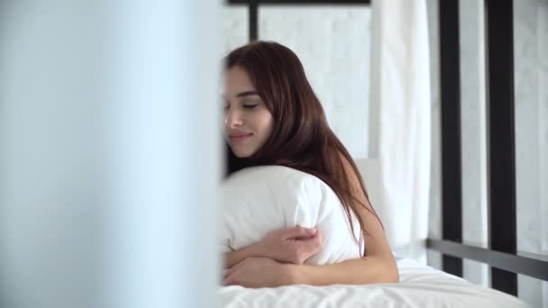 Hermosa mujer acostada en una cama cómoda y almohada abrazando — Vídeo de stock