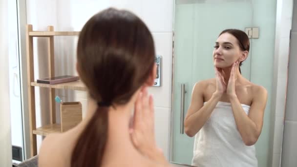 Cuidado de la piel. Mujer tocando la cara y mirando el espejo en el baño — Vídeo de stock