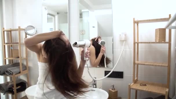 Уход за волосами. Женщина сушит длинные волосы с феном в ванной комнате — стоковое видео