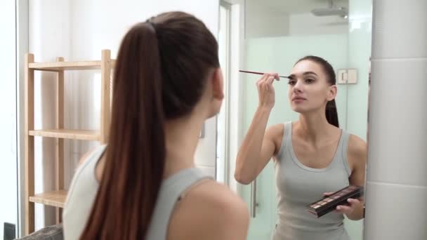 Maquillaje. Mujer aplicando sombras de ojos y mirando el espejo — Vídeos de Stock