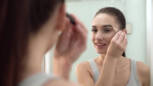 Maquiagem de beleza. Mulher escovando sobrancelhas no espelho do banheiro — Vídeo de Stock