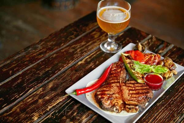 Steak And Beer. Barbecue Meat With Grill Vegetables And Beer On Table In Grill Restaurant. High Resolution