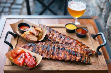 Barbekü kaburga ve bira Restoran Closeup tablo. Kaburga ızgara sebzeler ve sos ahşap tepsi. Yüksek çözünürlük