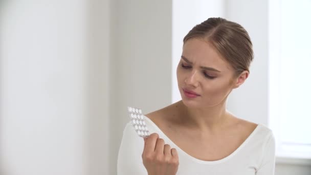Лекарства. Задумчивая женщина с таблетками в руке в белом интерьере — стоковое видео