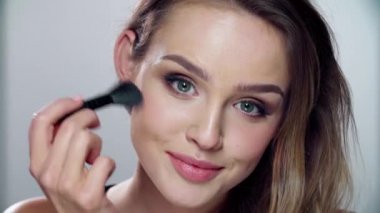 Güzel yüzlü bir kadın, fırçayla allık sürüyor.