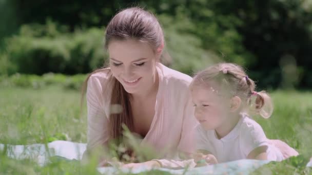 Junge Mutter und Tochter lesen Buch auf Gras im Park — Stockvideo
