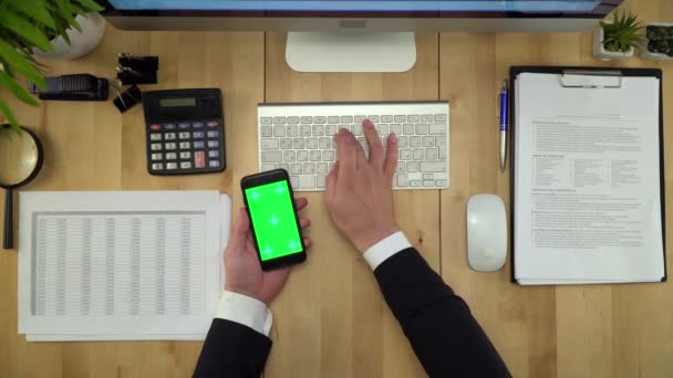Hombre de negocios usando el teléfono de pantalla verde y la computadora en la oficina — Vídeos de Stock