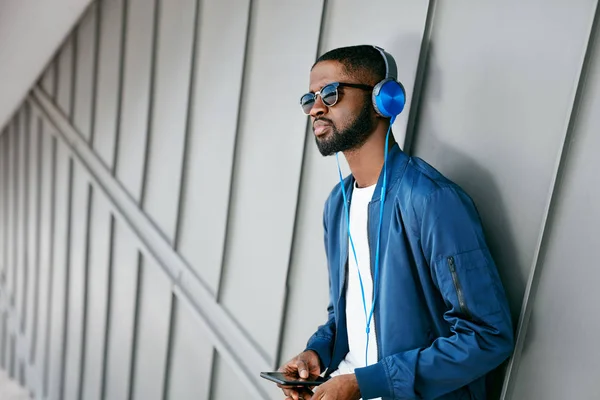 Moda e Música. Homem com fones de ouvido e telefone na cidade — Fotografia de Stock