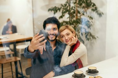 Telefonunuzun ve fotoğraf çekmek Cafe, mutlu insanlar. Güzel gülümseyen Çift görüntülü görüşme ile hareket eden telefon. Yüksek çözünürlük
