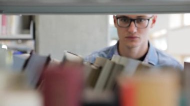 Üniversitedeki kütüphanede kitap arayan bir adam.