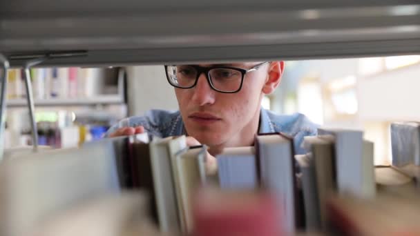Mann sucht Buch im Bücherregal der Bibliothek am College — Stockvideo