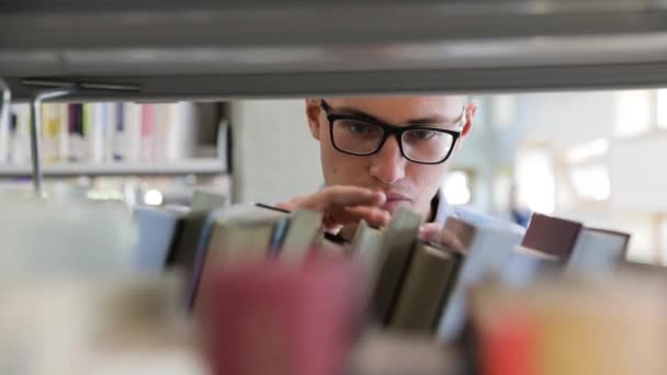 Man op zoek naar boek op boekenplanken in de bibliotheek op de universiteit — Stockvideo