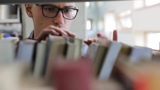 Homem à procura de livro em estantes na biblioteca na faculdade — Vídeo de Stock