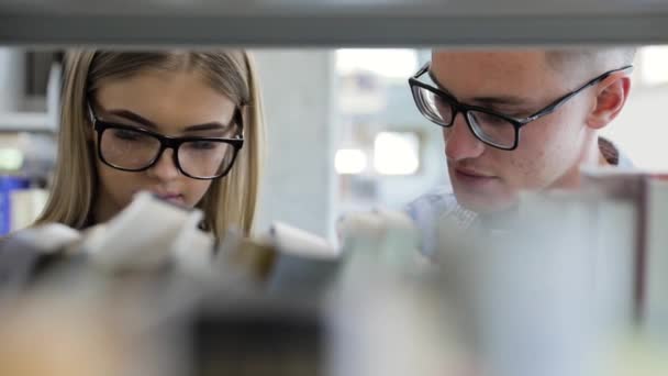 Studenten in bibliotheek zoeken leren boeken over boekenkasten — Stockvideo