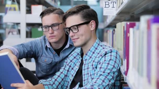 Estudantes lendo livro na biblioteca da faculdade perto de estantes — Vídeo de Stock