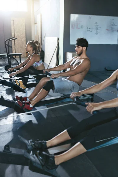 Crossfit. Gente haciendo ejercicio en la máquina de remo en el gimnasio de entrenamiento — Foto de Stock