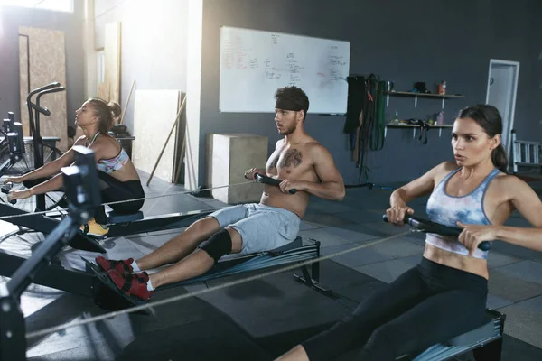 Crossfit. Gente haciendo ejercicio en la máquina de remo en el gimnasio de entrenamiento — Foto de Stock