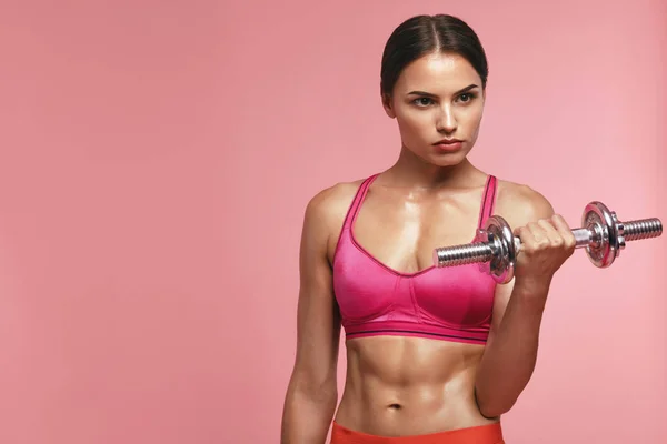 Culturismo. Mujer entrenando con mancuerna sobre fondo rosa — Foto de Stock