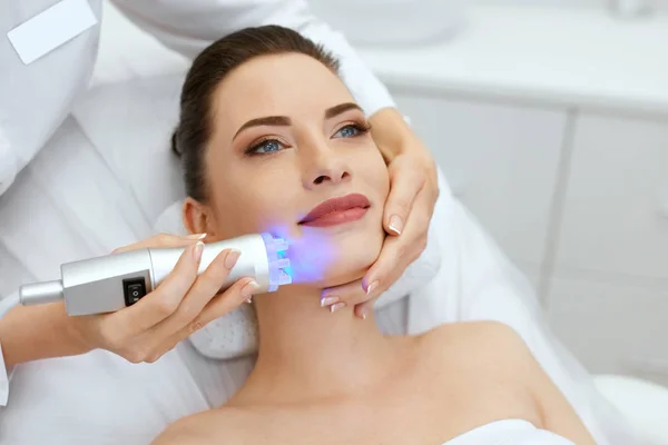 Gezicht huid cosmetologie. Closeup vrouw doen blauw licht behandeling — Stockfoto
