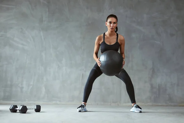 Mujer deportiva en ropa deportiva de moda se pone en cuclillas con pelota de fitness — Foto de Stock