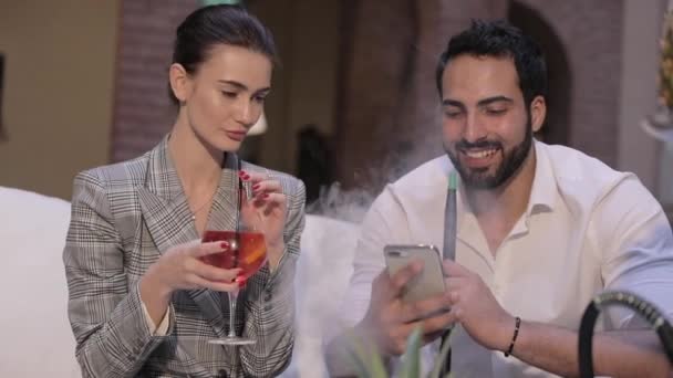 Hombre y mujer fumando Shisha, bebiendo cócteles y usando el teléfono — Vídeos de Stock