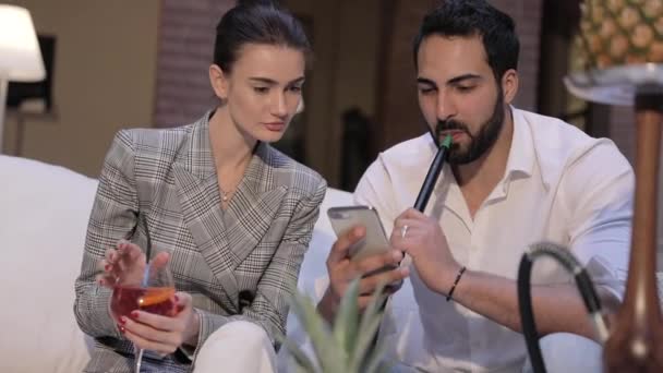 Mann und Frau rauchen Shisha, trinken Cocktails und telefonieren — Stockvideo