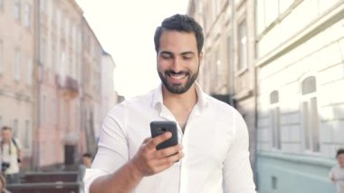 Adam cep telefonu kullanarak gülümseyen ve şehir cadde boyunca yürüyüş