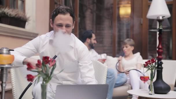 Бар Шиша. Человек курит кальян и работает за компьютером — стоковое видео