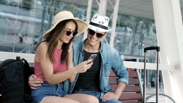 Cestování. Pár pomocí telefonu a sedící poblíž terminálu letiště — Stock video