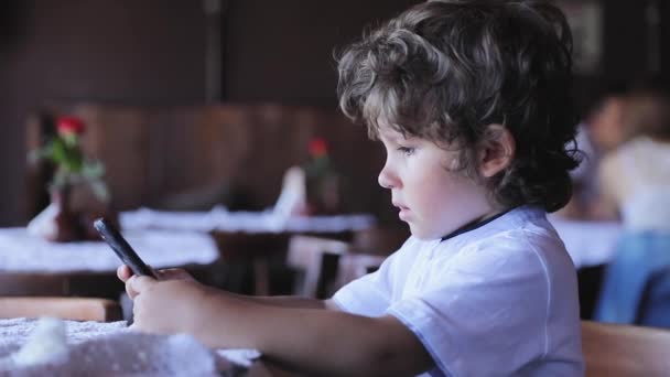 Niño pequeño con teléfono móvil en el café — Vídeos de Stock