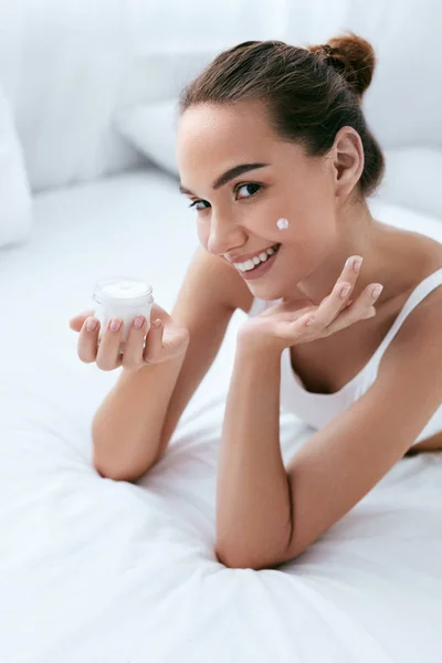 Crema facial de belleza. Hermosa chica sonriente aplicando crema en la piel — Foto de Stock