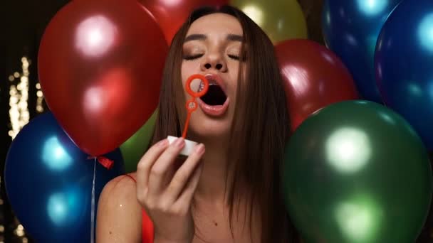 Oslava narozenin. Žena fouká mýdlové bubliny s balónky