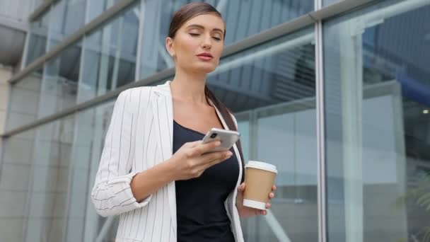 Ділова жінка з телефоном і кавою йде на роботу — стокове відео