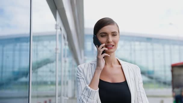 Vakker smilende kvinne som snakker i telefonen i nærheten av kontoret – stockvideo