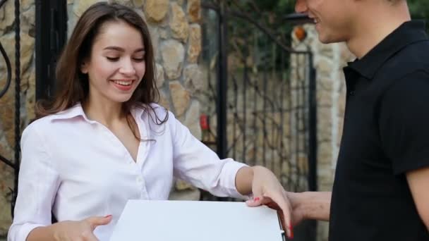 Доставка еды. Курьер дарит женщине коробку с пиццей на открытом воздухе — стоковое видео