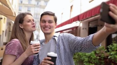 Telefonda fotoğraf çeken ve sokakta kahve içen bir çift.