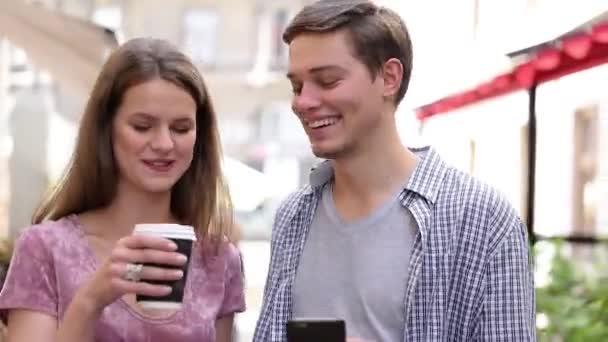 Gelukkige paar met behulp van de mobiele telefoon en koffie drinken buitenshuis — Stockvideo