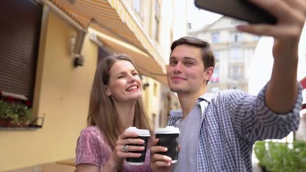 Para robi zdjęcie przez telefon i pije kawę na ulicy — Wideo stockowe