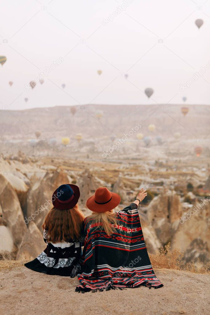 People Travel. Women In Hats Sitting On Hill Enjoying Flying Hot Air Balloons View At Cappadocia Turkey. High Resolution
