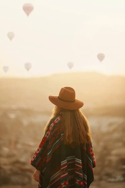 Ταξίδια. Γυναίκα με καπέλο με ιπτάμενα μπαλόνια στον ουρανό, το ηλιοβασίλεμα — Φωτογραφία Αρχείου