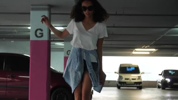 Belle femme dans les jeunes vêtements décontractés planche à roulettes au parking — Video