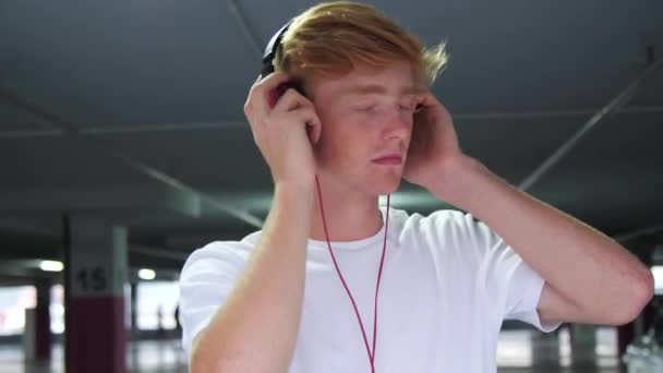 Rotschopf-Mann mit Kopfhörer hört Musik auf Parkplatz — Stockvideo