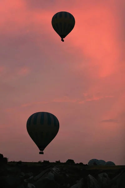 Siluetas de globos de aire caliente volando en el cielo rojo por encima del valle —  Fotos de Stock