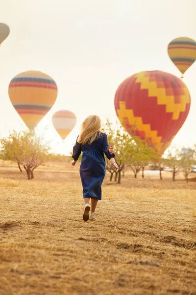 Mujer corriendo en el campo con globos de aire caliente volando —  Fotos de Stock