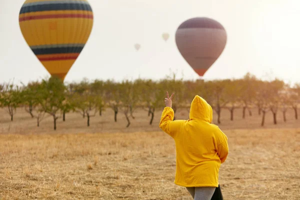 Viajar. Mujer mostrando paz con globos de aire caliente en el fondo —  Fotos de Stock